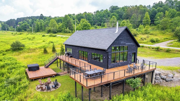 A modern house with a deck, large windows, and a staircase leading to the upper level. - Magnificent Chalet, Sweeping Views and Hot Tub (Ellicottville)