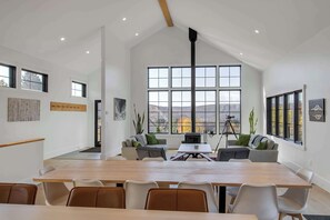 Una habitación amplia con una gran mesa de madera, varias sillas, un sofá y un ventanal con vistas a las montañas.