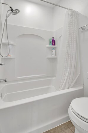 A bathroom with a bathtub, shower, toilet, and shelves with toiletries. - Magnificent Chalet, Sweeping Views and Hot Tub (Ellicottville)