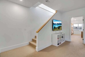 A modern staircase with a wooden handrail, a flat ceiling with recessed lighting, and a mounted television on a white console. - Magnificent Chalet, Sweeping Views and Hot Tub (Ellicottville)
