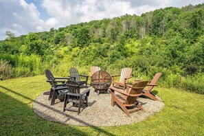 A circular outdoor seating area with Adirondack chairs and a fire pit, surrounded by a gravel circle, set against a backdrop of lush green forest. - Magnificent Chalet, Sweeping Views and Hot Tub (Ellicottville)