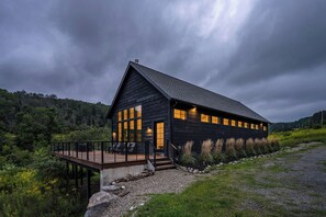 A large, dark wooden building with multiple windows, a deck, and a stone pathway leading to the entrance.