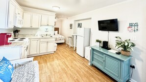 A compact kitchen with white cabinets, a microwave, a stove, and a sink. There's a ceiling fan, a TV mounted on the wall, and a small plant on the counter. - Oceanside Complex • Direct Beach Access  • Pool • Kitchen • Pet Friendly (Atlantic Beach)