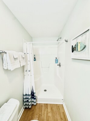 Une petite salle de bain propre, équipée d’une douche, de toilettes et d’un porte-serviettes.
