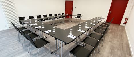 Un salón de conferencias con una larga mesa, sillas negras y una puerta roja.