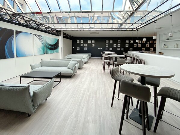 A modern interior with a glass ceiling, light-colored flooring, and a mix of sofas and tables.