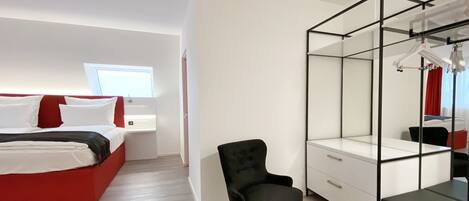 A modern hotel room with a bed, a chair, a wardrobe, and a window.