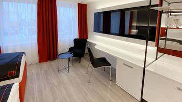 A modern hotel room with a bed, a desk, a chair, and a small table.
