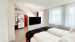 A modern hotel room with a bed, a TV mounted on the wall, and a view of the outside through large windows. - DORMERO Hotel Hersbruck (Hersbruck)