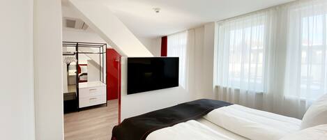 Un hotel moderno con una cama, un televisor montado en la pared y vistas al exterior a través de amplias ventanas.