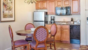 Una cocina con armarios de madera, un refrigerador, un microondas y una cafetera. Hay una mesa de comedor con cuatro sillas.