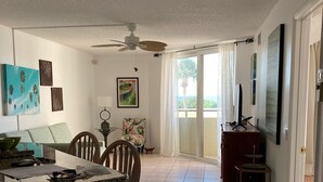A spacious living area with a dining table, chairs, a ceiling fan, and a view through a sliding glass door.