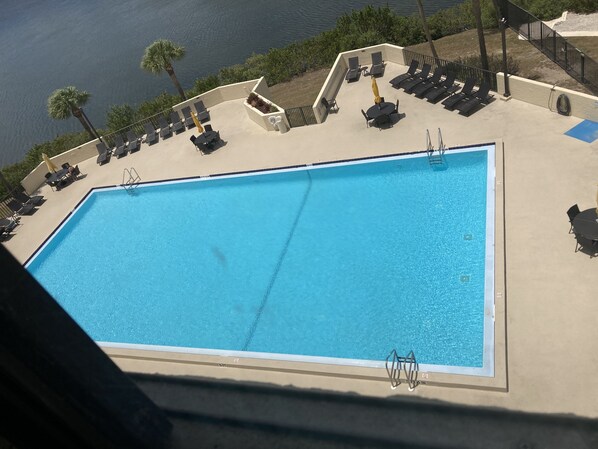 Una piscina rectangular con superficie de agua azul cristalina, rodeada de sillas de descanso y una pequeña mesa con un paraguas amarillo.