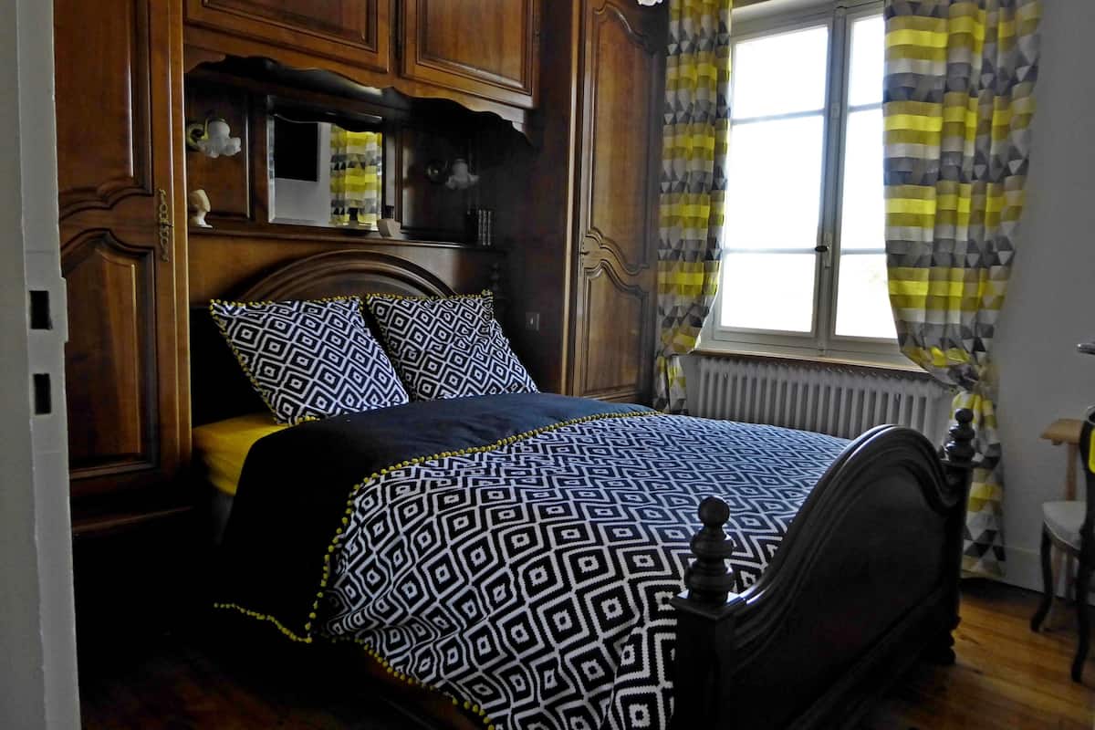 A bedroom with a bed, wooden headboard, and a window with curtains.