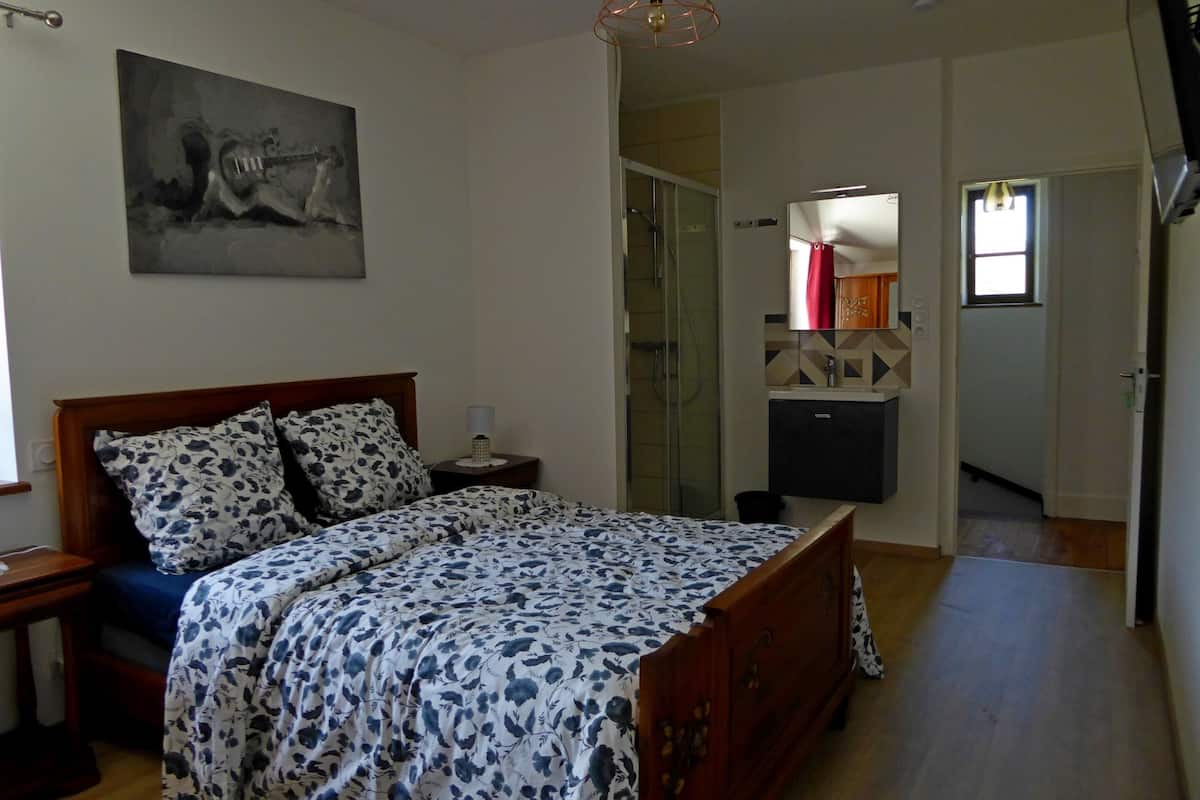 A bedroom with a wooden bed, a nightstand, a bedside table, a mirror, and a painting on the wall.