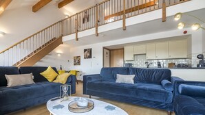 Een ruime woonkamer met twee donkerblauwe banken, een marmeren bijzettafeltje en een houten trap.