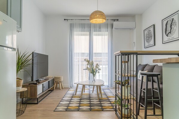A modern kitchen with a large TV, a dining table with chairs, and a hanging light fixture.
