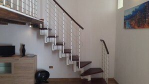 A modern staircase with a wooden handrail and white steps, leading to a landing with a flat-screen TV and a small cabinet. - CASA PETRA - OPEN SPACE (brindisi)