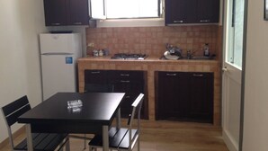 A compact kitchen with a dining table, chairs, a refrigerator, a stove, and cabinets. - CASA PETRA - OPEN SPACE (brindisi)