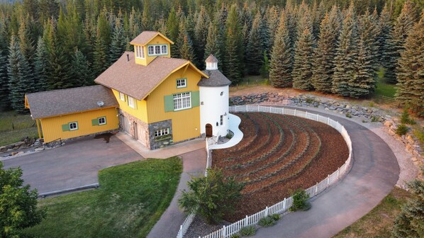 A yellow house with a white tower, surrounded by a circular driveway and a forested area.