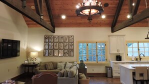 A spacious kitchen with wooden beams, a chandelier, a dining area with a table and chairs, and a large window with a view of trees. - Gorgeous Home and Property Located Just 30 Minutes From Glacier National Park (Kalispell)