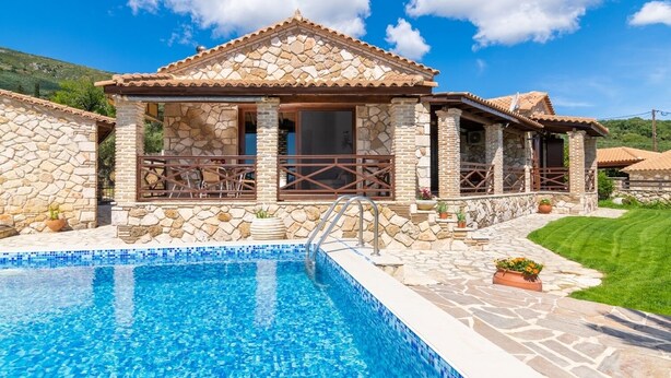 Une villa en pierre dotée d’une piscine, comprenant un patio aménagé avec du mobilier d’extérieur et un chemin en pierre menant à la piscine.