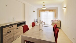 A modern living room with a dining area, featuring a wooden dining table, red chairs, a sofa, and a television. - Prestige For Home - 2 bedroom apartment - Lagos (Lagos)