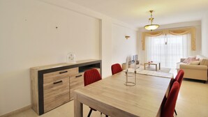 A modern living room with a dining area, featuring a wooden dining table, red chairs, a sofa, and a TV. - Prestige For Home - 2 bedroom apartment - Lagos (Lagos)