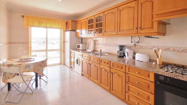 A kitchen with wooden cabinets, a dining table with chairs, a washing machine, and a gas stove. - Prestige For Home - 2 bedroom apartment - Lagos (Lagos)