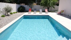 A rectangular swimming pool with clear blue water, surrounded by a white wall and a gravel area.