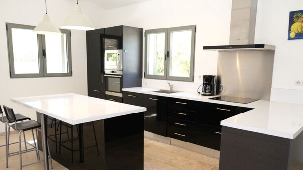 A modern kitchen with a central island, black cabinetry, and a stainless steel range hood.