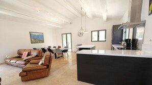A spacious living area with a brown leather sofa, a dining table with chairs, a kitchen area with a black countertop, and a large window providing natural light.