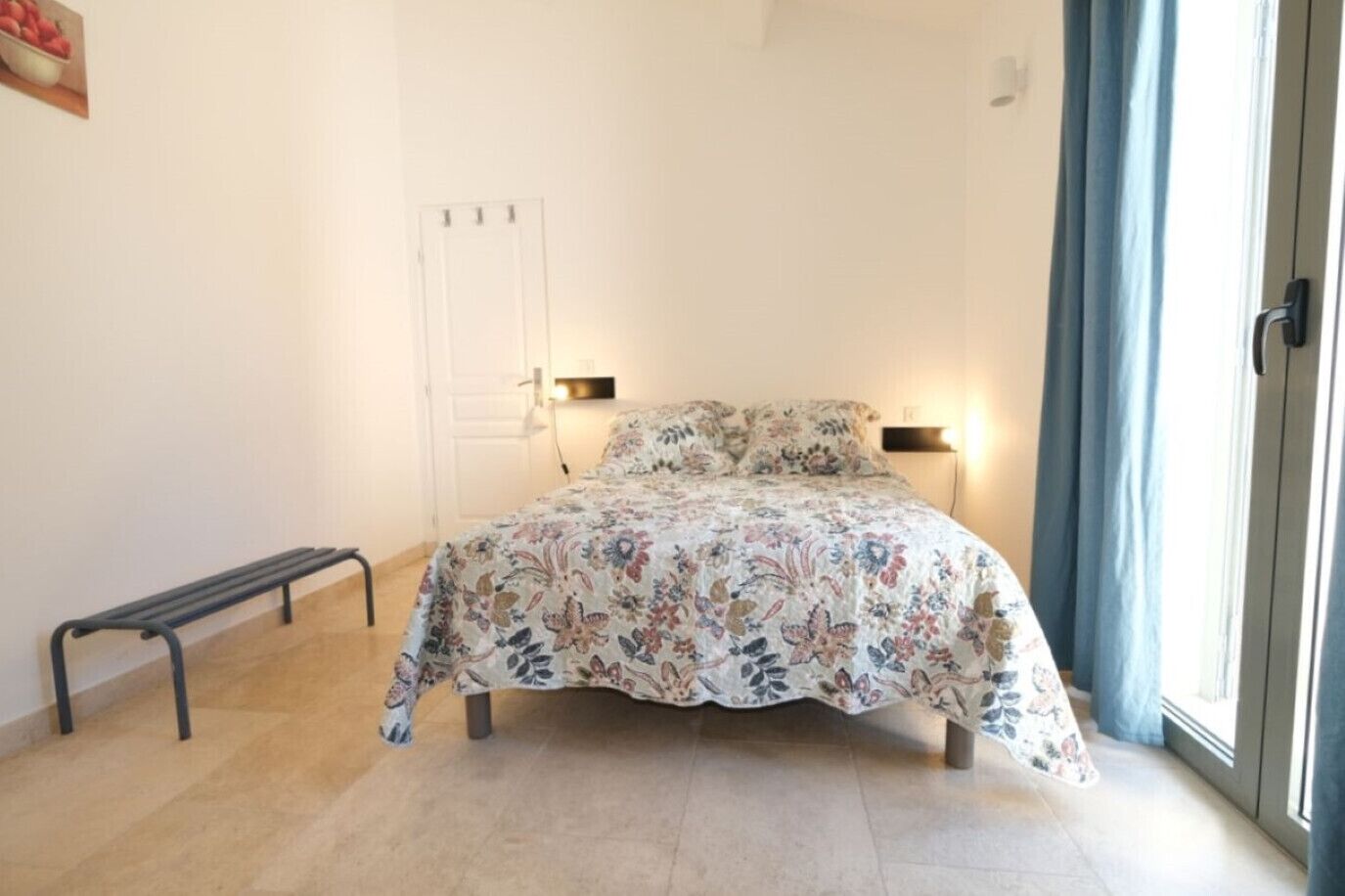 Una camera da letto con un letto, lampade sui comodini, una panca e una porta.