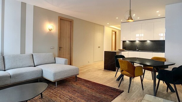 Ein modernes Wohnzimmer mit einer Eckcouch, einem Esstisch mit Stühlen und einer Küchenzeile mit schwarzer Arbeitsplatte und weißen Schränken.