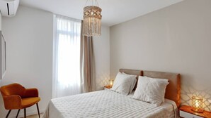 Ein modernes Schlafzimmer mit einem großen Bett, einem Holznachttisch, einem kleinen Tisch, einem Stuhl und einer Pendelleuchte.