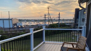 Eine Holzterrasse mit zwei Stühlen und einem Tisch, mit Blick auf einen Yachthafen mit Booten und einer fernen Küstenlinie.