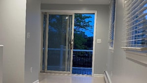 Ein Flur mit einer Schiebetür, die auf einen Balkon mit Blick auf Bäume und einen Zaun führt.