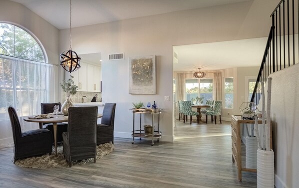 A spacious dining area with a round table and chairs, a kitchen in the background, and a staircase leading to another level.