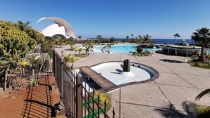 A resort pool area with a central fountain, palm trees, and a distinctive building with a curved roof.