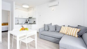 A modern living room with a grey sofa, white table, and a kitchen area in the background.