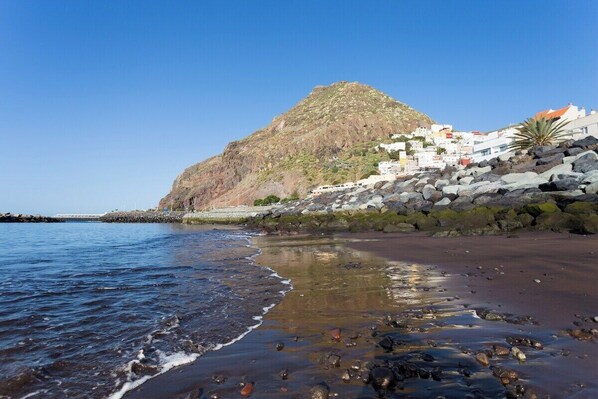 A coastal town with white buildings on a rocky hillside, a beach with pebbles, and calm sea waves. - Home2Book Sea Front Las Teresitas Beach 5 (San Andres de Tenerife)