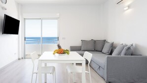 Un salon moderne avec une table blanche, un canapé gris et une grande fenêtre donnant sur la mer.