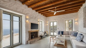 A spacious living room with a stone fireplace, a white sofa, and a large window overlooking the sea. - Infinity Villa, luxury house with stunning view in Serifos (Serifos)