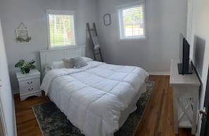 A bedroom with a large bed, two bedside tables, a TV, and a window with blinds. - Gables Miami Home with HEATED SALT POOL. Near Beaches, Airport and Night life (Coral Gables)