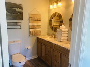 Een badkamer met toilet, wastafel en houten kastjes. Er is een handdoekrek met handdoeken en een spiegel met houten omlijsting.