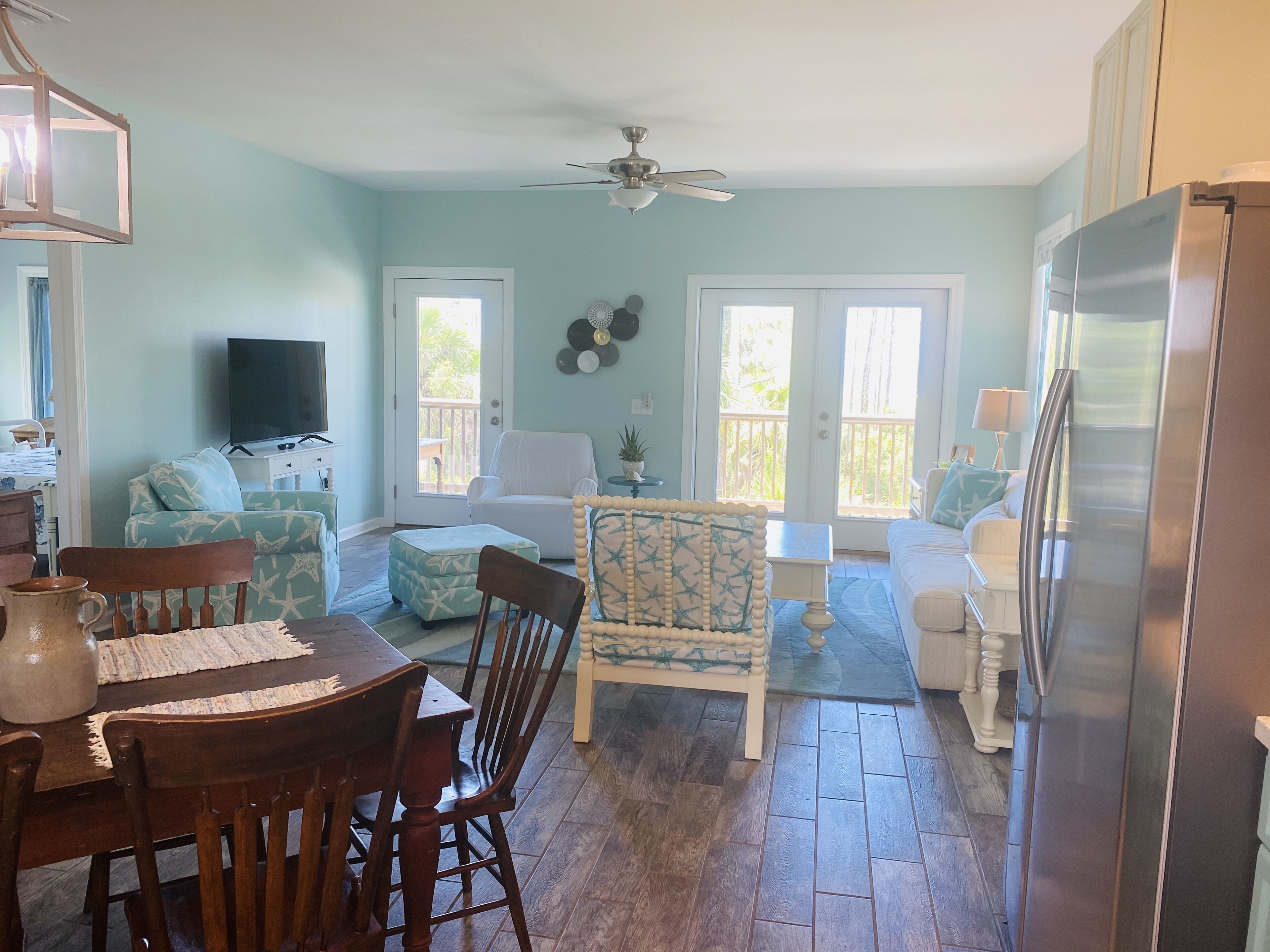 A spacious living area with a dining table, chairs, a sofa, and a TV. There are two doors leading to a balcony.