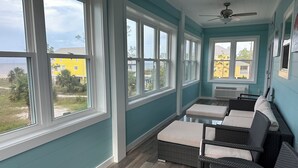Aurinkoinen huone, jossa on suuret ikkunat, rottingista valmistetut huonekalut ja kattotuuletin.