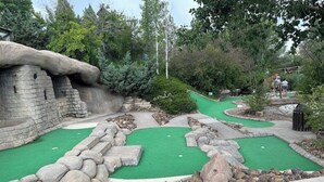 En minigolfbane med en stengul struktur, grøn kunstgræs og en stenkant.
