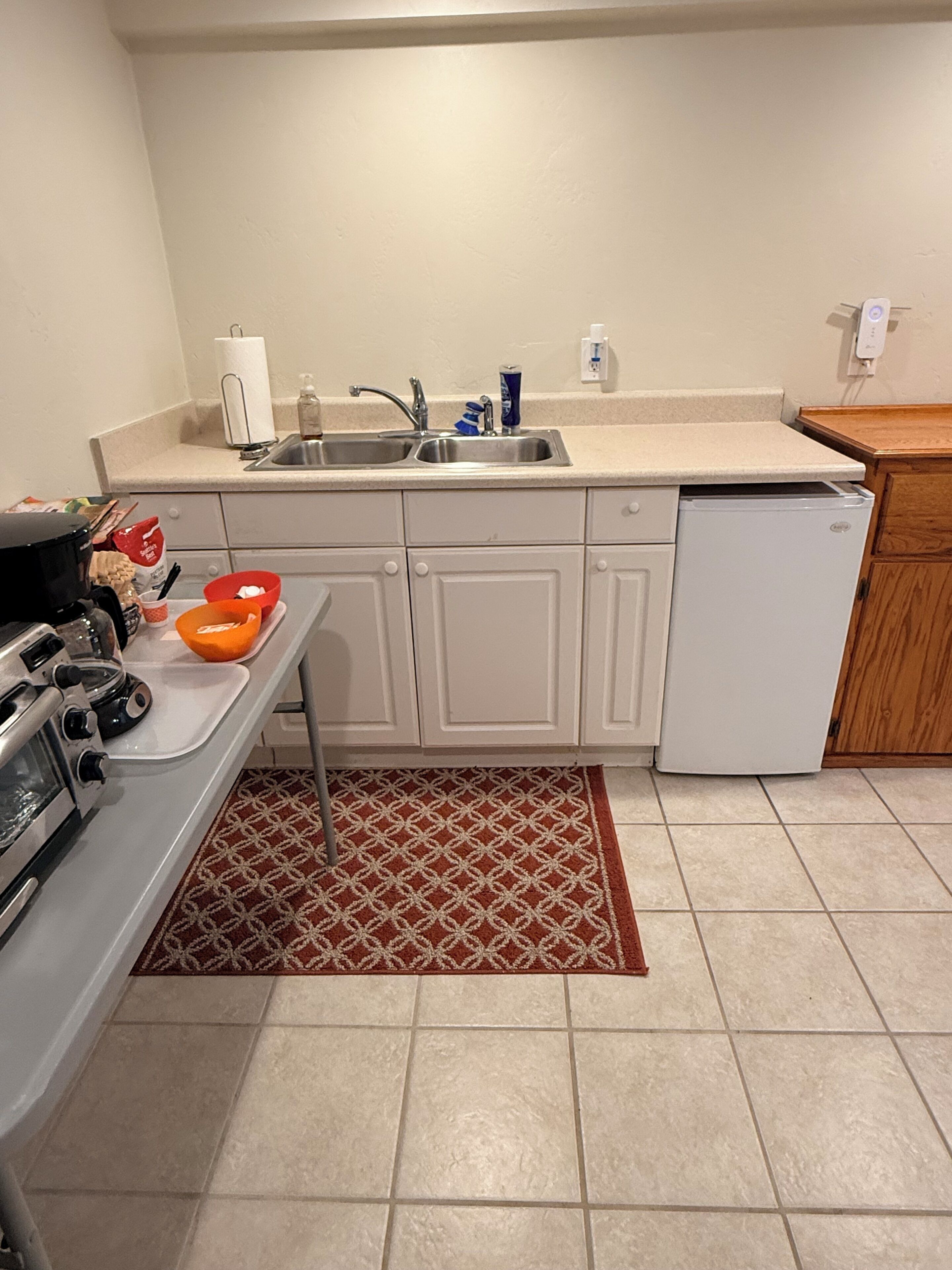 A compact kitchen with a stove, sink, and refrigerator, featuring a patterned rug and tiled flooring.
