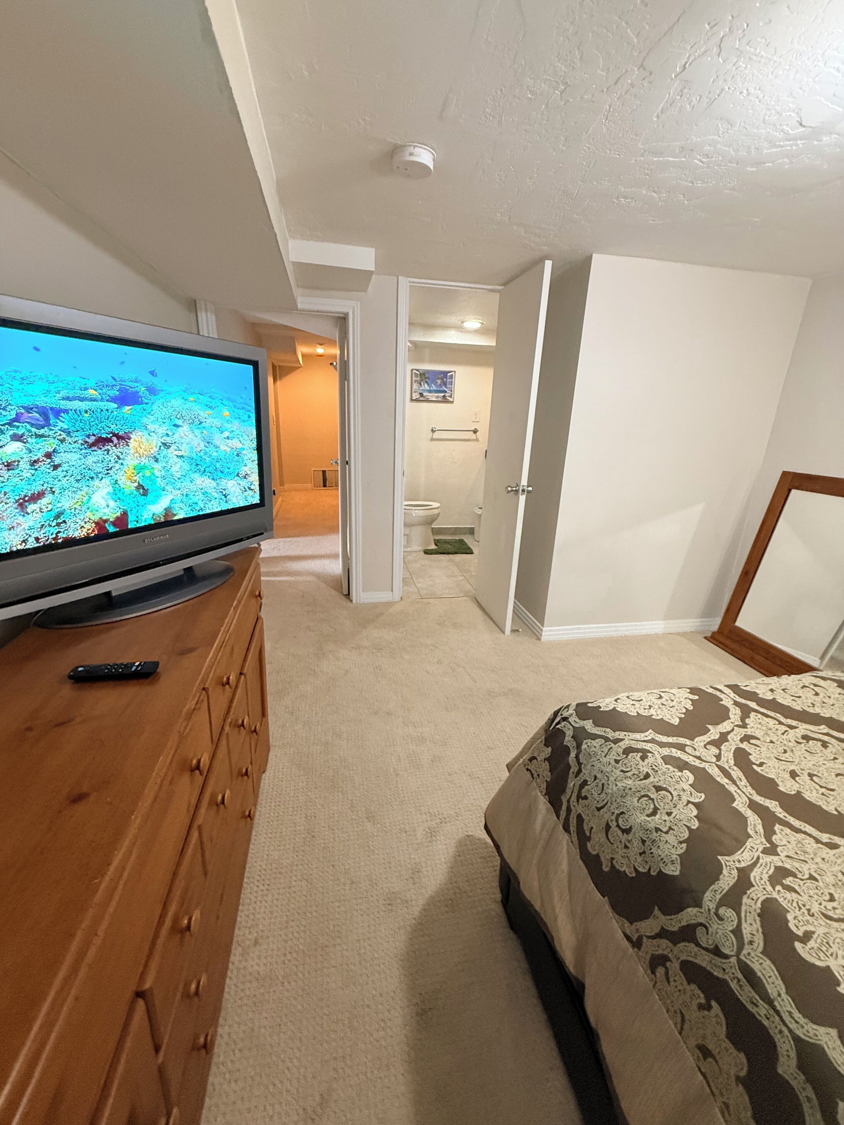 A bedroom with a TV on a wooden dresser, a bed with patterned bedding, and a bathroom visible through an open door.